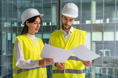 Ofiste çalış. Sarı yelekli ve kalın şapkalı iki kişi ofiste birlikte çalışıyor.