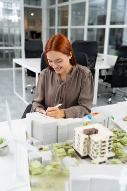 - Mimar. Genç beyaz kadın mimar ofiste bir bina modeli üzerinde çalışıyor.
