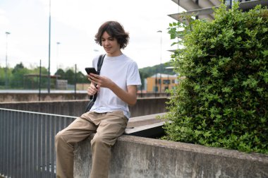 İletişim. Elinde telefon olan beyaz tişörtlü genç adam memnun görünüyor.