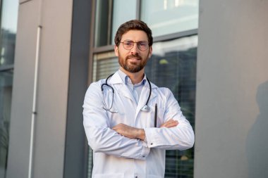 Kendine güven. Gözlüklü erkek doktor kolları bağlı duruyor.