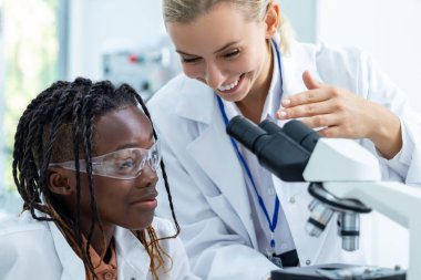 Mikroskopla çalış. Beyaz laboratuardaki sarışın öğretmen bir öğrenciye mikroskopla nasıl çalışacağını anlatıyor.