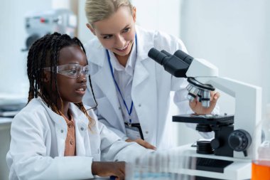 Mikroskopla çalış. Beyaz laboratuardaki sarışın öğretmen bir öğrenciye mikroskopla nasıl çalışacağını anlatıyor.