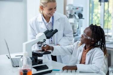 Mikroskopla çalış. Beyaz laboratuardaki sarışın öğretmen bir öğrenciye mikroskopla nasıl çalışacağını anlatıyor.