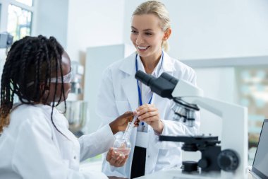 Mikrobiyoloji. Laboratuvar önlüklü sarışın kadın bir öğrenciye mikroskobu nasıl dava edeceğini anlatıyor.