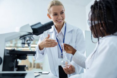 Mikrobiyoloji. Laboratuvar önlüklü sarışın kadın bir öğrenciye mikroskobu nasıl dava edeceğini anlatıyor.