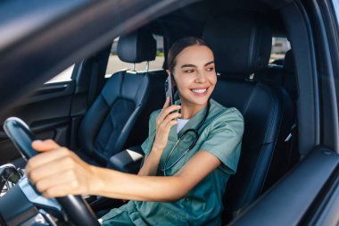 Telefondaki hemşire. Ameliyat kıyafetli genç bir kadın arabada oturuyor ve telefonda konuşuyor.