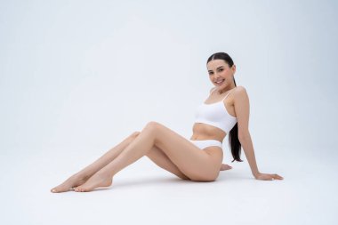 Güzel kadın. Beyaz iç çamaşırlı, uzun saçlı, tatlı bir kadın yerde oturuyor ve gülümsüyor.