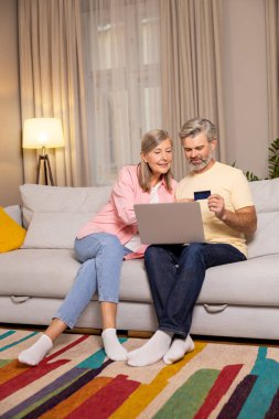 İnternetten alışveriş. Kanepede yan yana oturan olgun bir çift internette ödeme yapıyor.