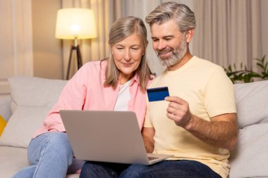 İnternetten alışveriş. Kanepede yan yana oturan olgun bir çift internette ödeme yapıyor.