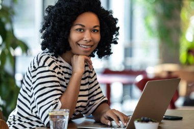 Serbest çalışan biri. Kumral kıvırcık saçlı kadın bir kafede otururken dizüstü bilgisayarla çalışıyor.