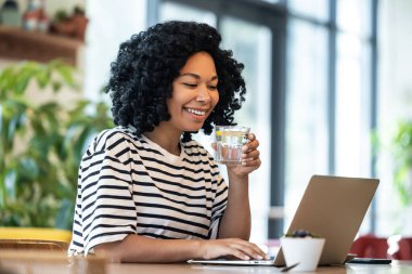 Serbest çalışan biri. Kumral kıvırcık saçlı kadın bir kafede otururken dizüstü bilgisayarla çalışıyor.