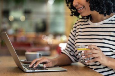 Serbest çalışan biri. Kumral kıvırcık saçlı kadın bir kafede otururken dizüstü bilgisayarla çalışıyor.