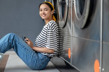 Kişisel hizmet. Genç tatlı kız çamaşırhanenin yanında yerde oturuyor ve bekliyor.