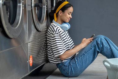 Kişisel hizmet. Genç tatlı kız çamaşırhanenin yanında yerde oturuyor ve bekliyor.