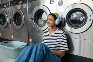 Kişisel hizmet. Genç tatlı kız çamaşırhanenin yanında yerde oturuyor ve bekliyor.