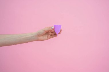 Mor silikon regl bardağını pembe arka planda tutan tanınmamış bir kadın eli.