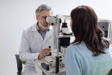 Objektif muayenesi için optometri merkezini ziyaret eden kadın görüş durumunu değerlendirmek için gelişmiş lamba kullanıyor.