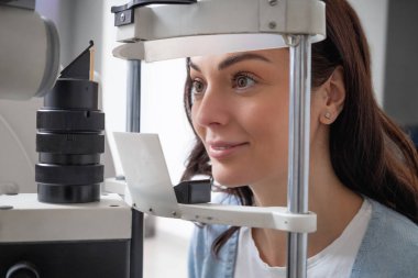 Optometri kliniğindeki kadın hasta görüşünü uygun gözlük ve lens düzeltmesi için ölçüyor.