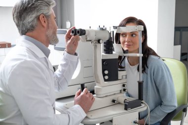 Objektif muayenesi için optometri merkezini ziyaret eden kadın görüş durumunu değerlendirmek için gelişmiş lamba kullanıyor.