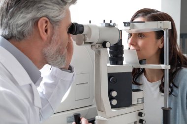 Optik klinikte teşhis için kadın hasta vizyonunu profesyonel ekipmanla muayene eden erkek doktor