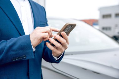 Tanımlanamayan takım elbiseli işadamı, otomobil endüstrisinde güvenli satışlarda akıllı telefon tutuyor.