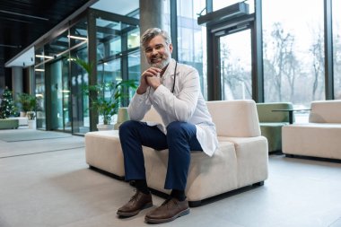 Meslektaşımı bekliyorum. Laboratuvar önlüklü gülümseyen doktor klinik salonundaki koltukta oturuyor.