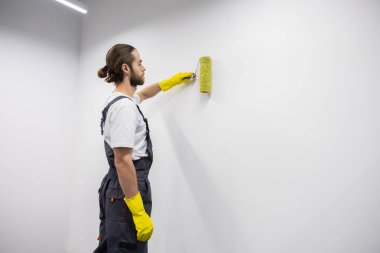 Duvarları boyuyorum. Siyah saçlı, sakallı, sarı eldivenli, duvarı boyayan genç adam.