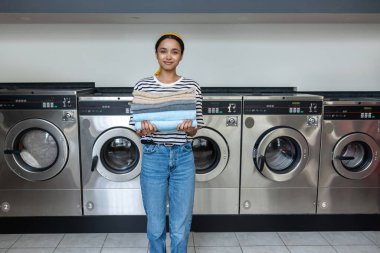 Çamaşırhanedeki esmer kadın kurutucuda kuruttuktan sonra temiz havluları istiflemiş.