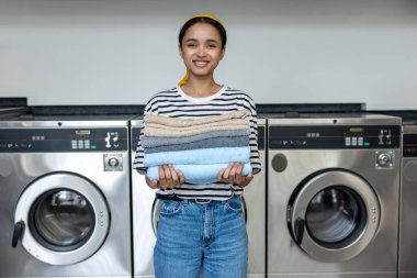 Çamaşır makinesini havlularını temizlemek için kullandıktan sonra çamaşırhanede gülümseyen bir kadın.