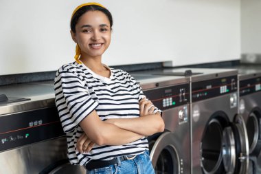 Çamaşır makinesindeki kadın kurutma makinesinin çalışmasını beklerken çamaşır makinesiyle çamaşırlarını yıkıyor.