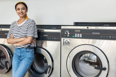 Çamaşır makinesindeki kadın kurutma makinesinin çalışmasını beklerken çamaşır makinesiyle çamaşırlarını yıkıyor.