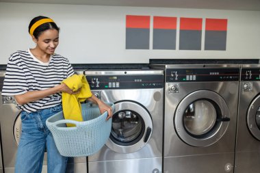 Çamaşırhanede kirli çamaşırlarını yıkamak için çamaşır makinesi kullanan bir kadın.