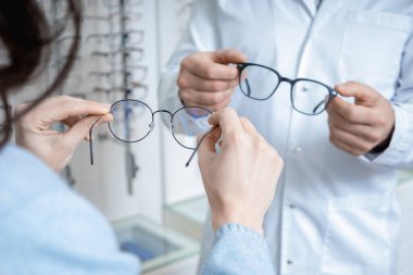 Farklı gözlükler. Optik mağazasında bir müşteriye gözlük gösteren bir gözlük asistanı