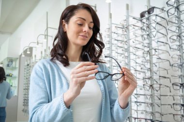 Yeni gözlük. Genç siyah saçlı kadın optik dükkanında yeni gözlük deniyor.
