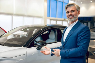 Profesyonel sakallı satıcı galeride yeni bir araba sunuyor.