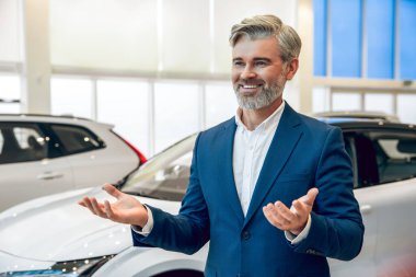 Profesyonel sakallı satıcı galeride yeni bir araba sunuyor.