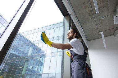 Ofiste servis var. Ofisteki pencereleri temizleyen ve meşgul görünen genç bir servis elemanı.
