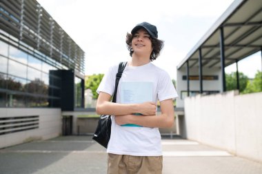 Kişisel gelişim, bilgi, eğitim. Sırt çantalı genç bir üniversite öğrencisi kampüste yürüyor ve kitap okuyor.