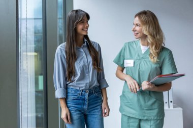 Klinikte beyaz kadın teşhisci hastalarla konuşuyor. Koridorda belgeleri kontrol ediyorlar.