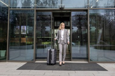 İş gezisi. Güzel takım elbiseli zarif sarışın kadın bir bavul taşıyor.