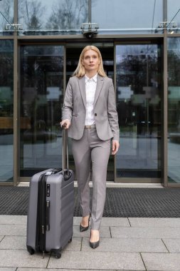 İş gezisi. Güzel takım elbiseli zarif sarışın kadın bir bavul taşıyor.