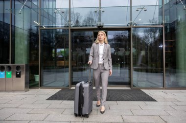 İş gezisi. Güzel takım elbiseli zarif sarışın kadın bir bavul taşıyor.