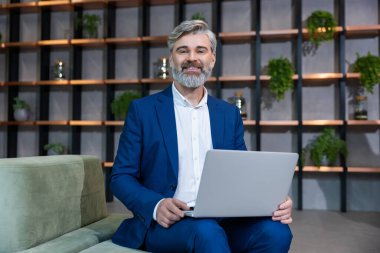 İş adamı. Gri saçlı, iş yerinde şık takım elbiseli, olgun bir iş adamı.