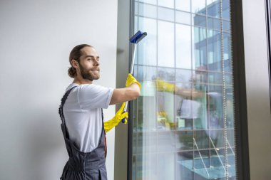 Pencere temizliği. Pencereyi temizleyen genç adam pencere temizleyicisiyle