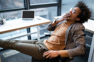 Takım elbiseli bir işadamı büyük pencereli bir ofiste oturuyor.