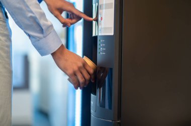 Modern ofis mutfağında çalışan tanınmayan genç bir iş adamı kahve yapıyor.