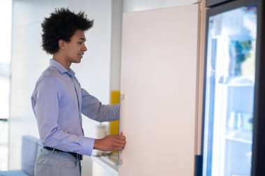 Afro saçlı genç işadamı modern ofisin mutfağında kahve hazırlıyor.