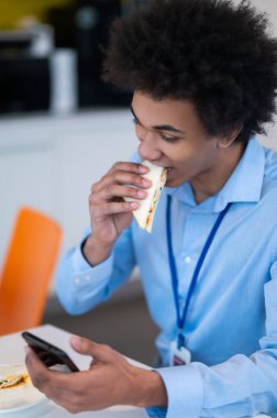 Aç adam yemek yiyor ve internetten akıllı telefondan ofis mutfağına kayıyor.