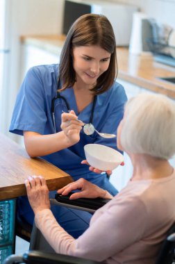 Hasta bakıcı, hasta olduğu sırada evde çorba içmesine yardım ediyor.