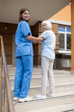 Yaşlı bir hastayla yürüyen kadın hemşire emekliliğe destek olmak için baston kullanıyor.